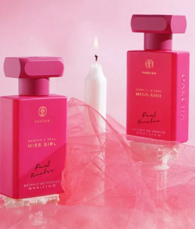 Two pink perfume bottles labeled 'Miss Girl' on a pink background with a candle.